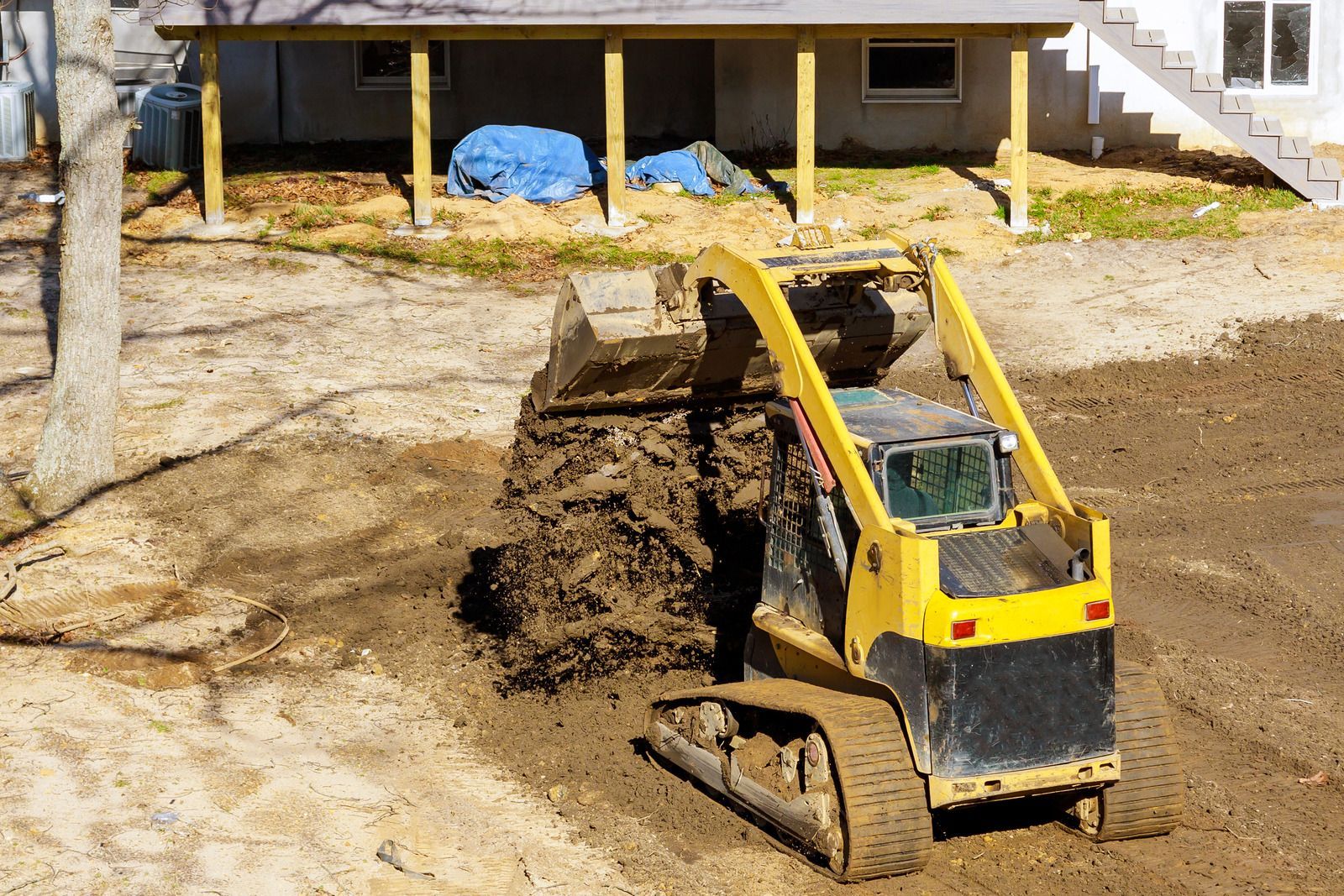 Yellow mini excavator dumping dirt at a construction site outdoors