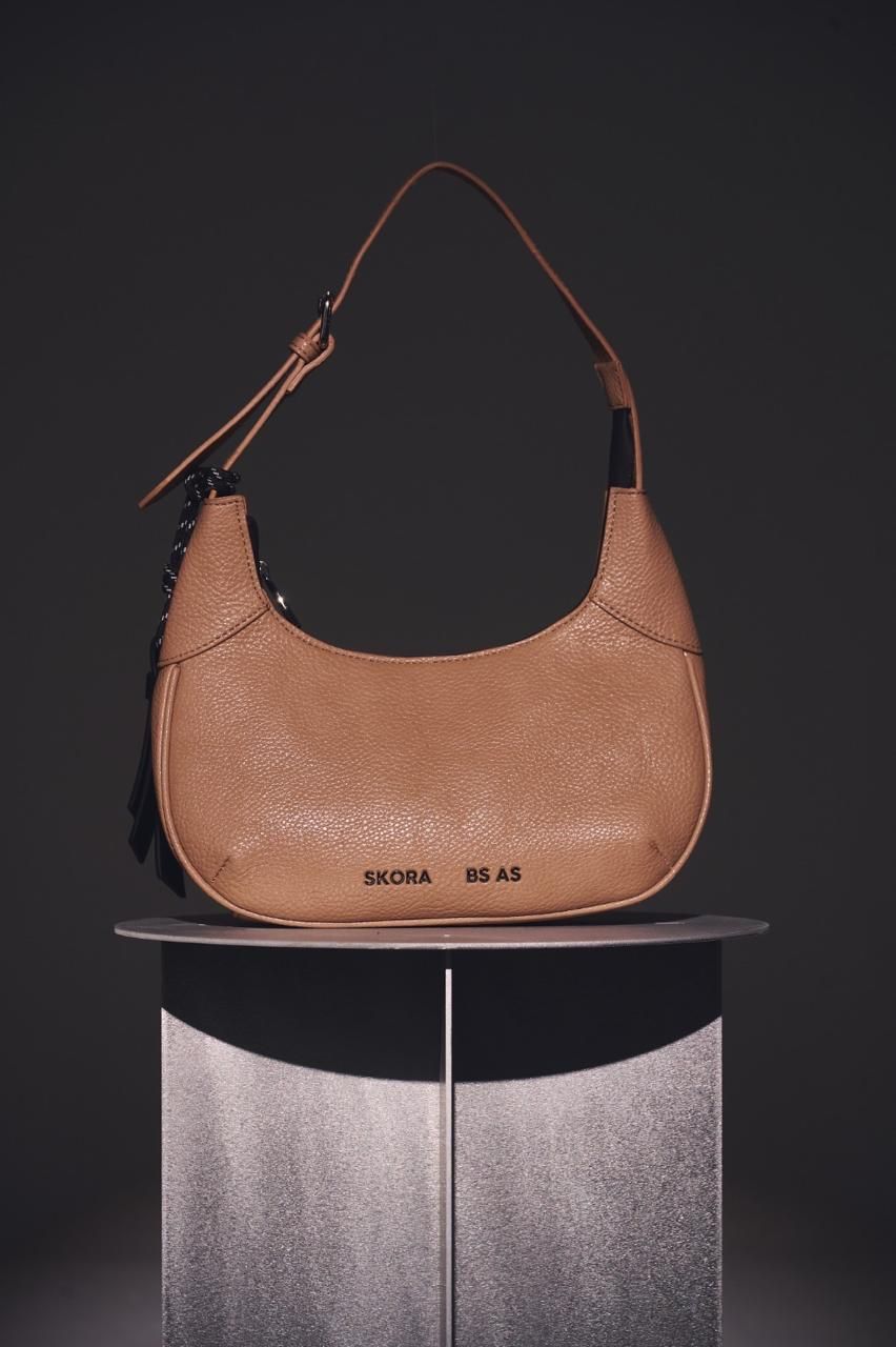 Un bolso de mano color canela, texturizado y con forma de media luna, con una correa corta para el hombro.