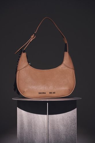 Un bolso de mano color canela, texturizado y con forma de media luna, con una correa corta para el hombro.