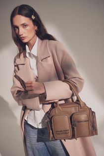 Una persona que viste un abrigo rosa pálido y una camisa blanca sostiene un bolso marrón.