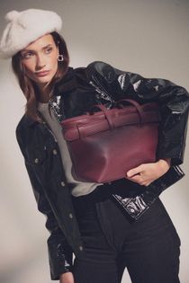 Una persona que lleva una boina blanca y una chaqueta de vinilo negra posa mientras sostiene un bolso de cuero.