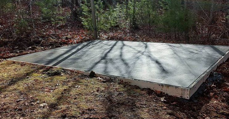 Freshly poured concrete slab on grade.  The slab is in a backyard surrounded by a forested area.