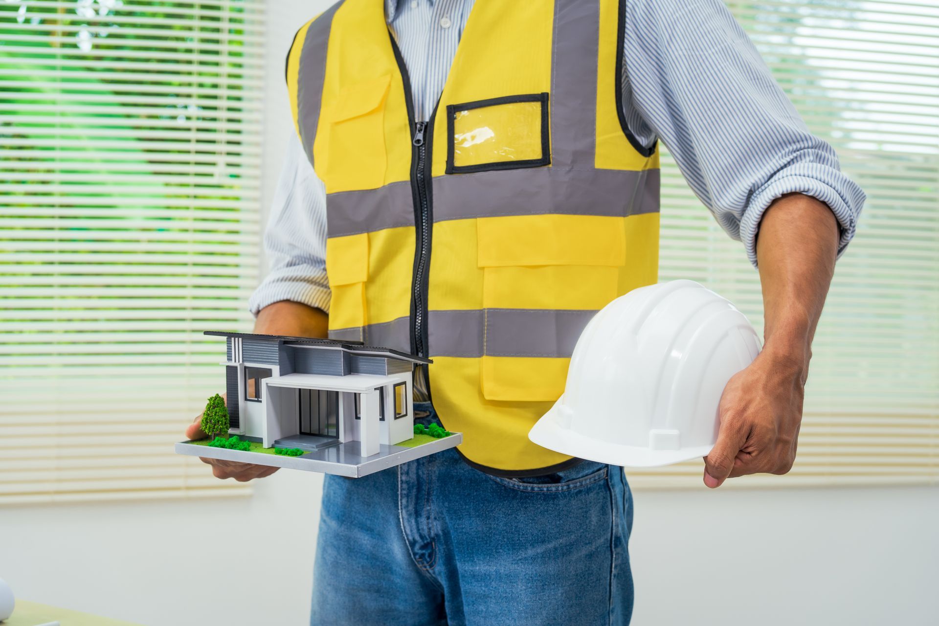 A construction worker is holding a model house and a hard hat.