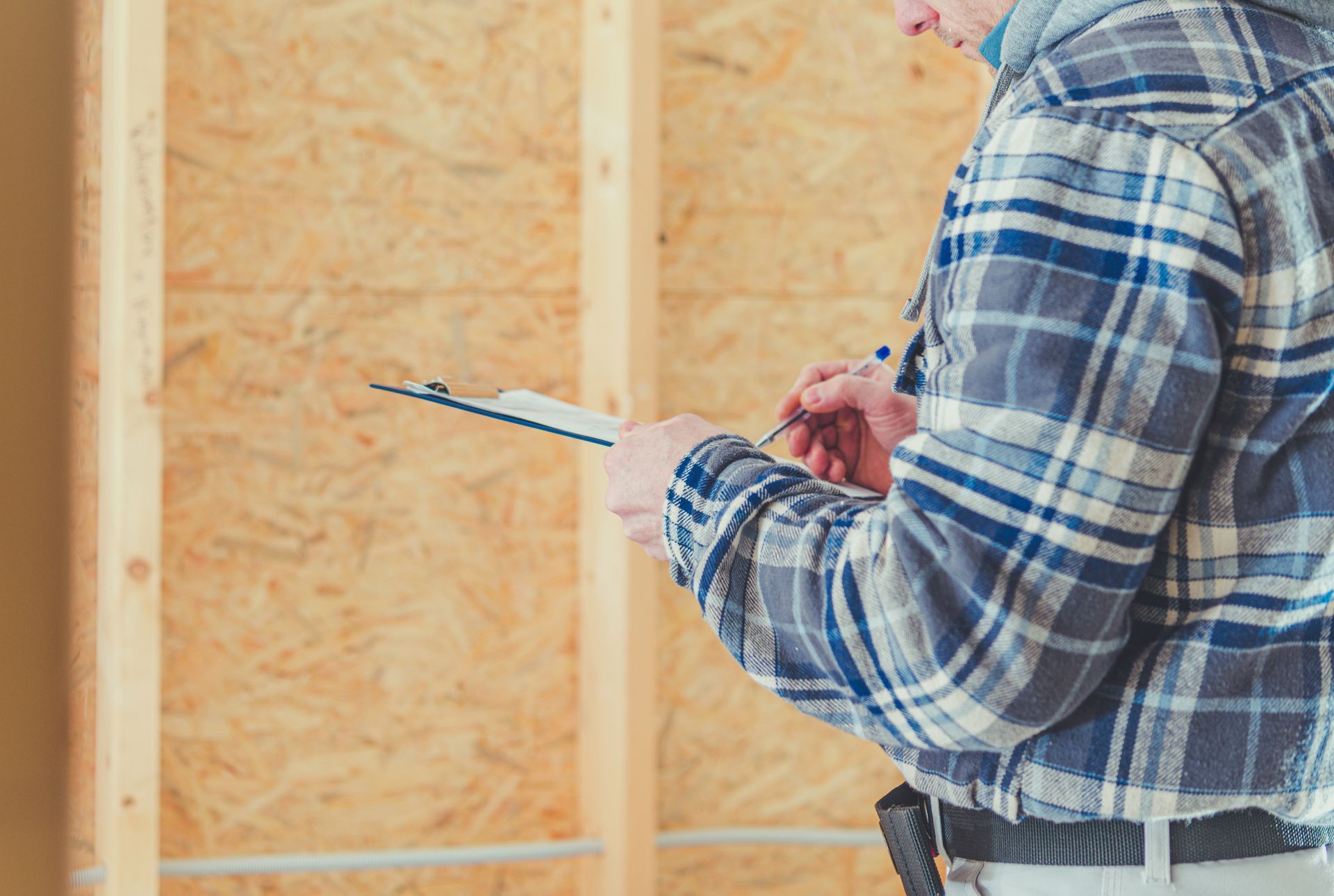 A man in a plaid shirt is holding a clipboard and writing on it.