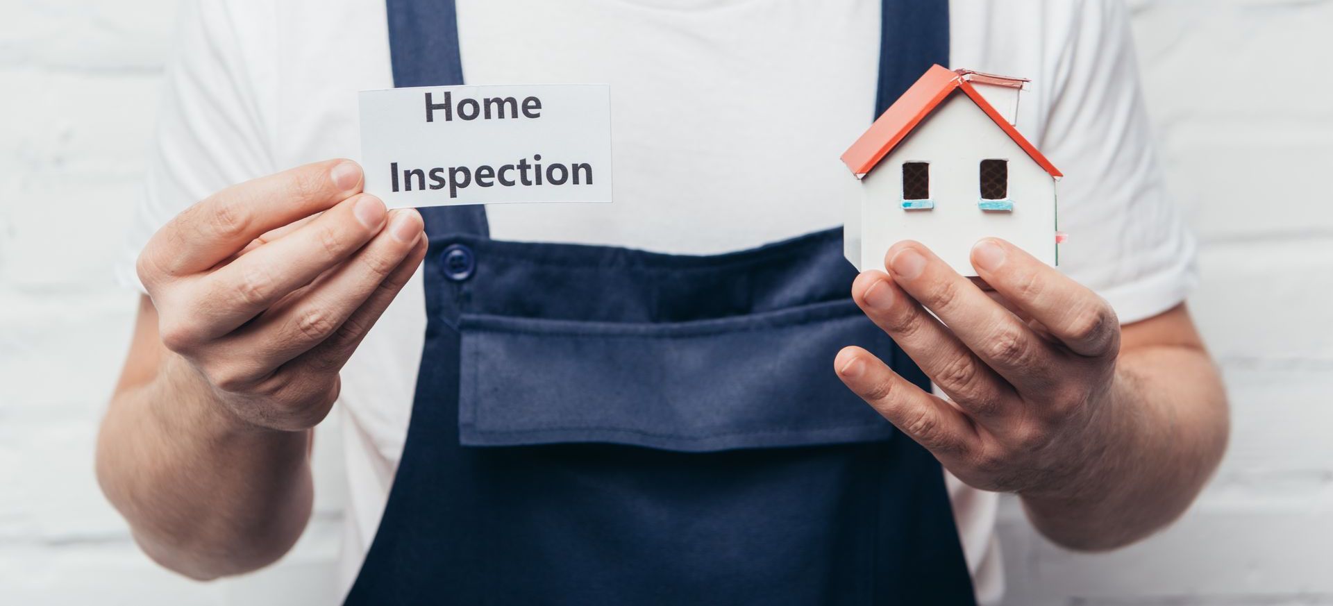 A man is holding a small model house and a sign that says `` home inspection ''.