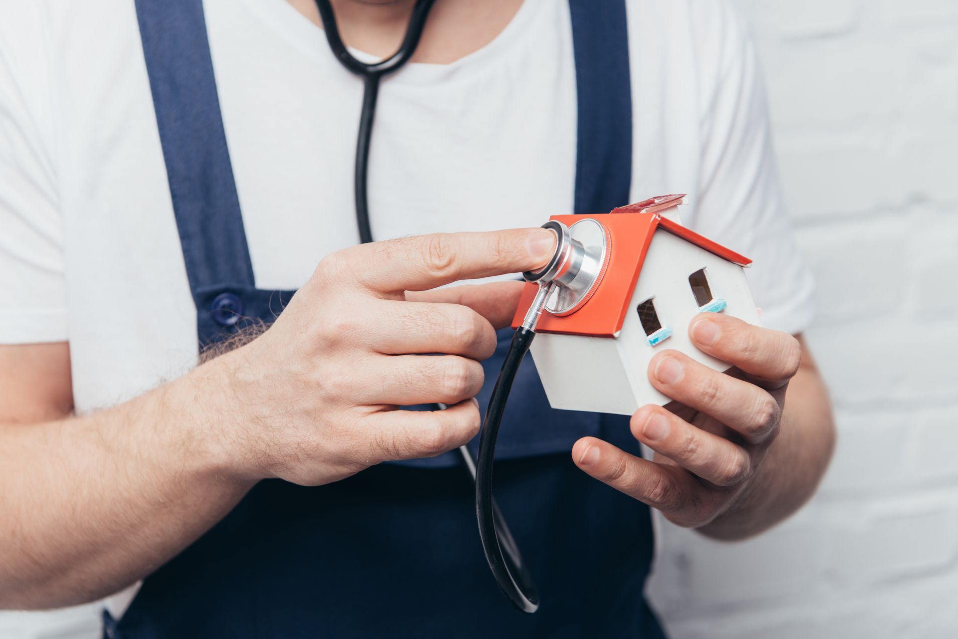 A man is holding a model house with a stethoscope around his neck.