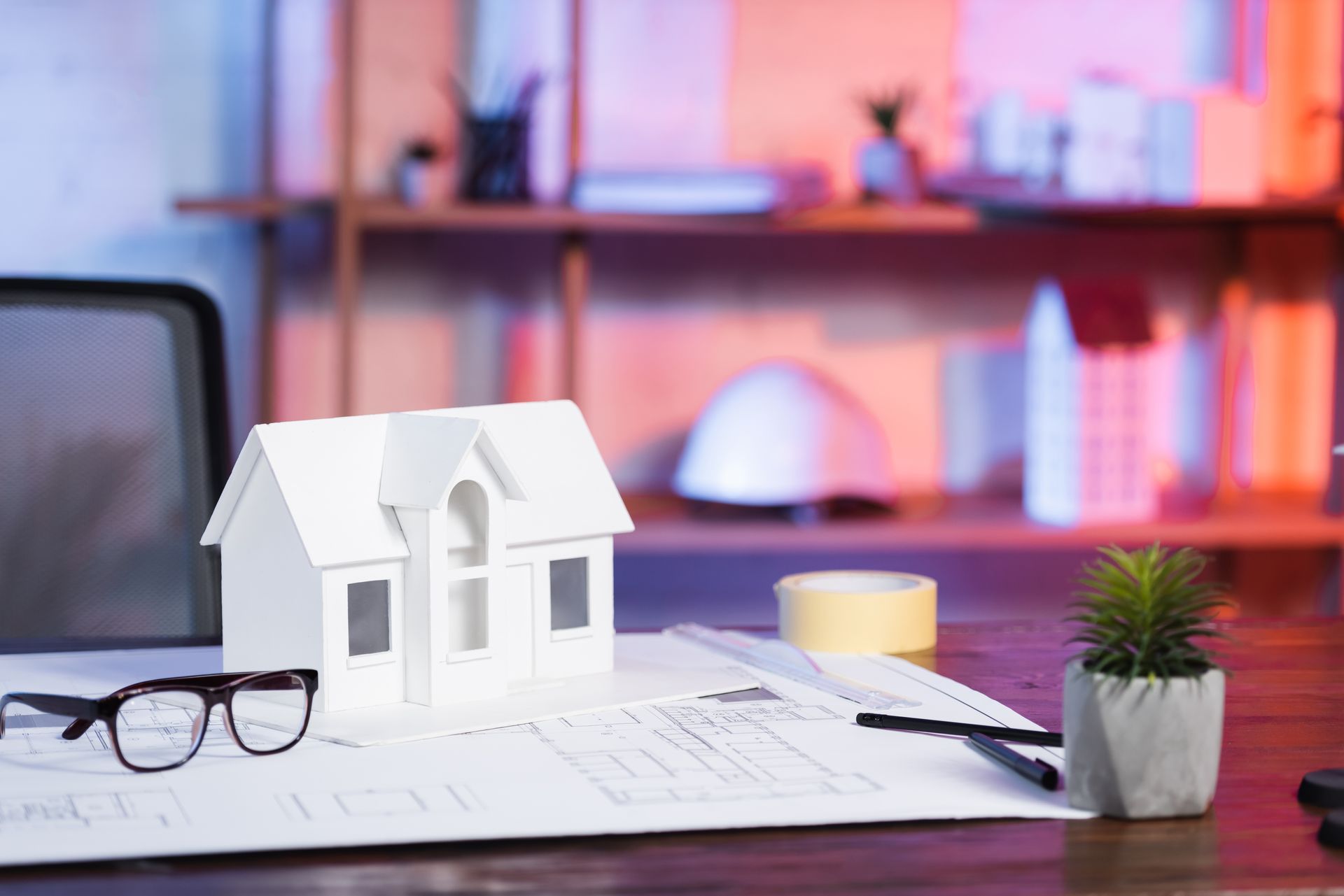 A model house is sitting on top of a desk next to a pair of glasses.