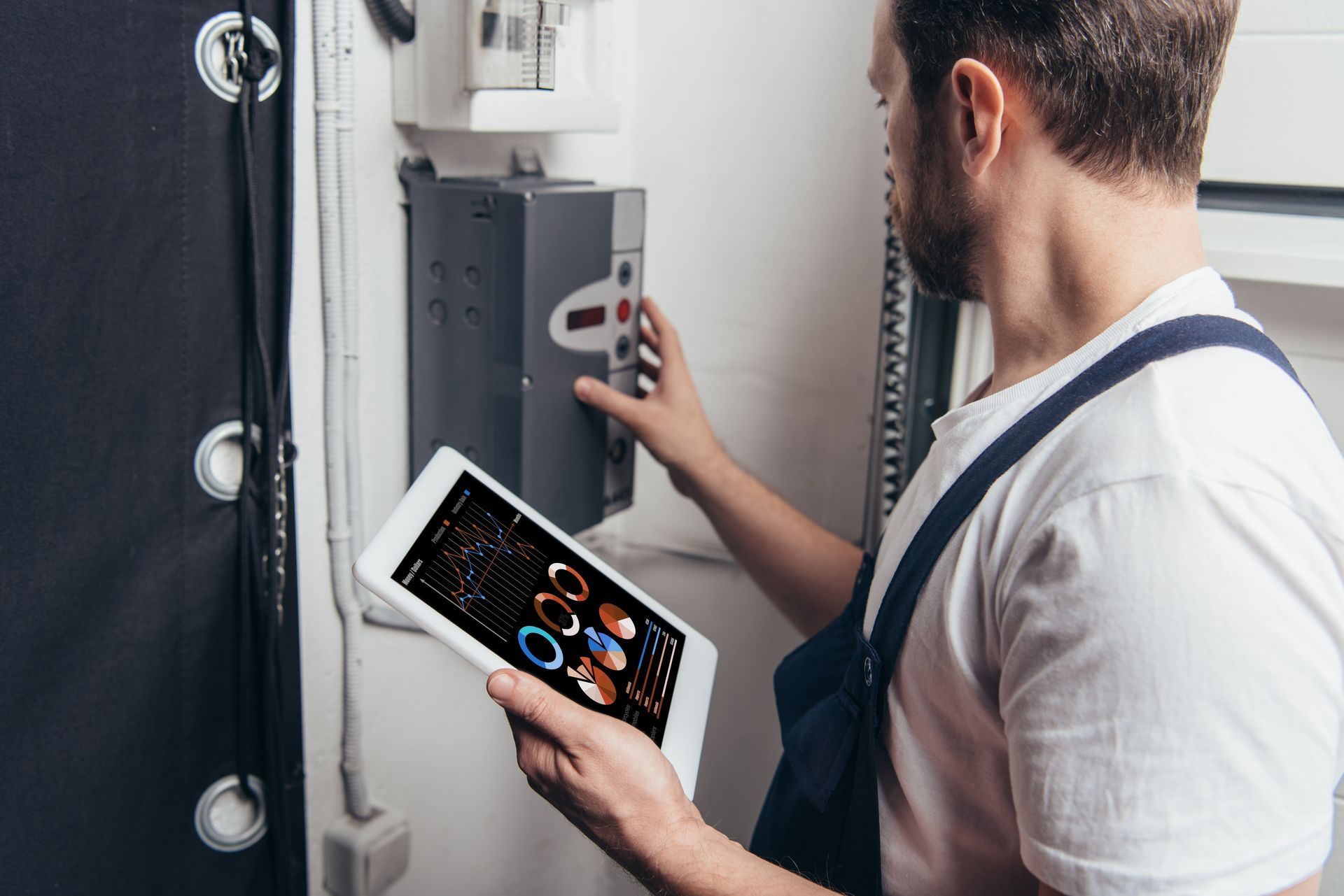 A man is holding a tablet in his hand while working on an electrical box.