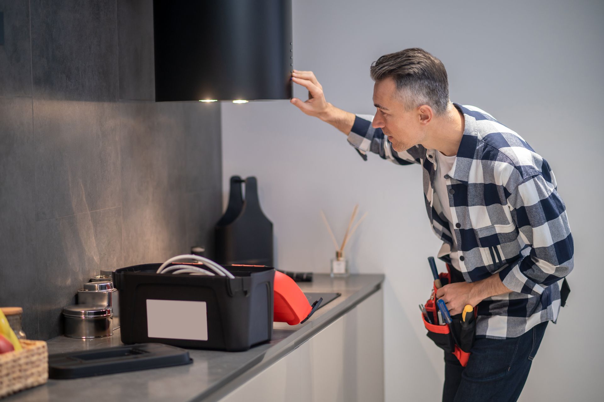 A man is fixing a hood in a kitchen.