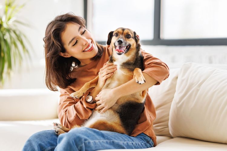 Woman in brown shirt and jeans holds a happy dog
