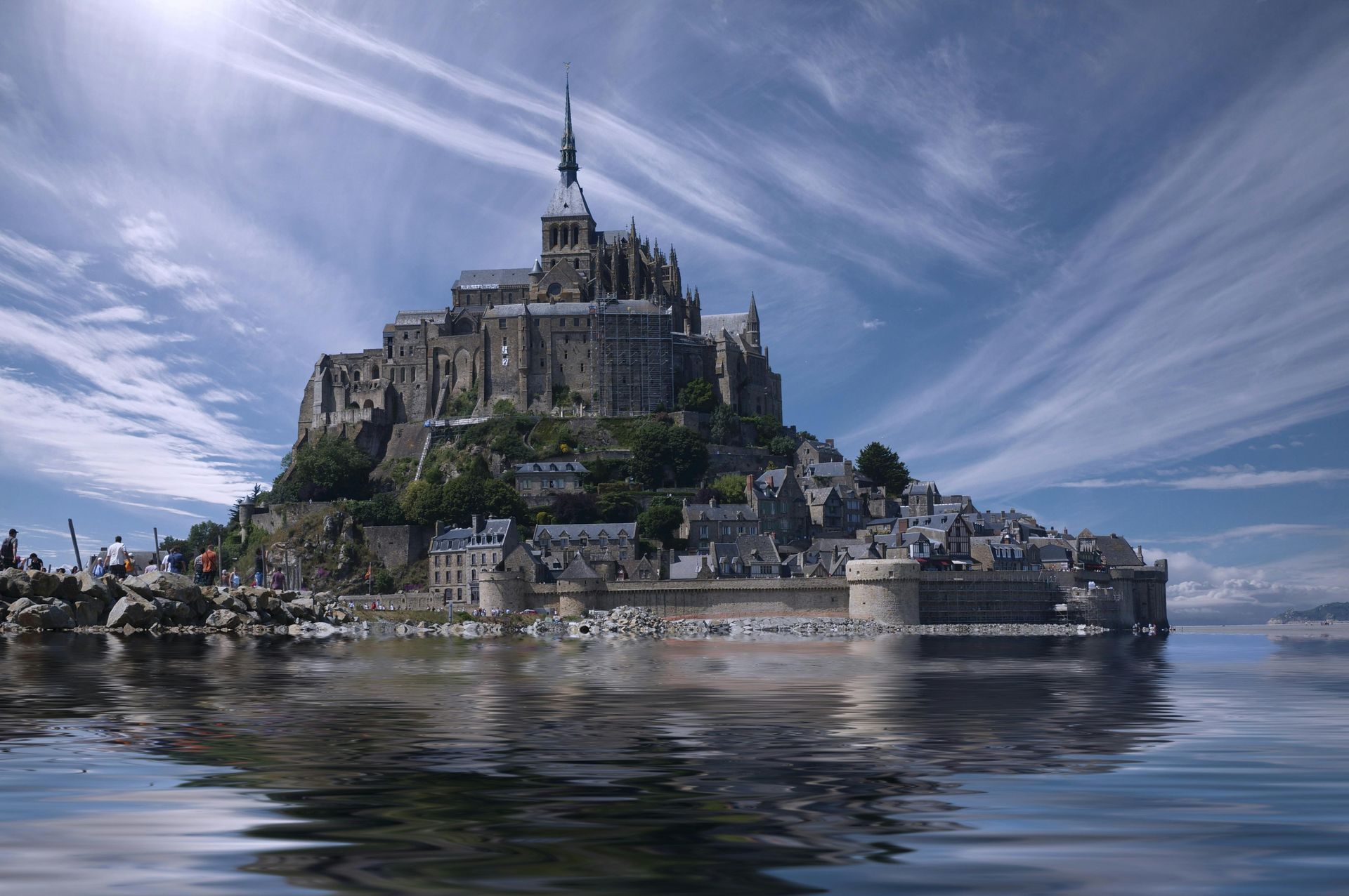 Mont Saint-Michel, France, rising from the water, under a bright, cloudy sky; stone architecture.