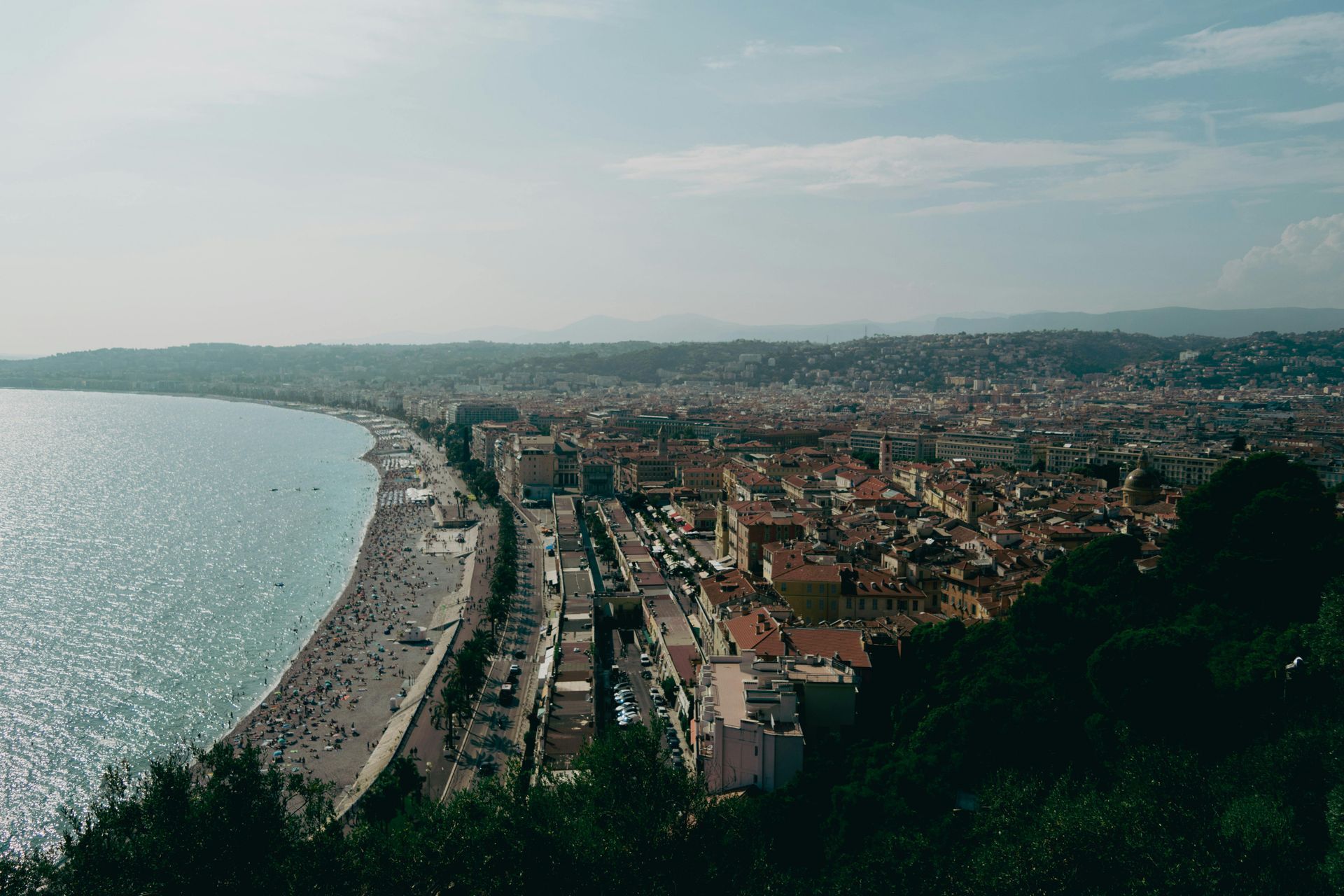 Coastal city view with a beach, buildings, and a hillside under a hazy sky.