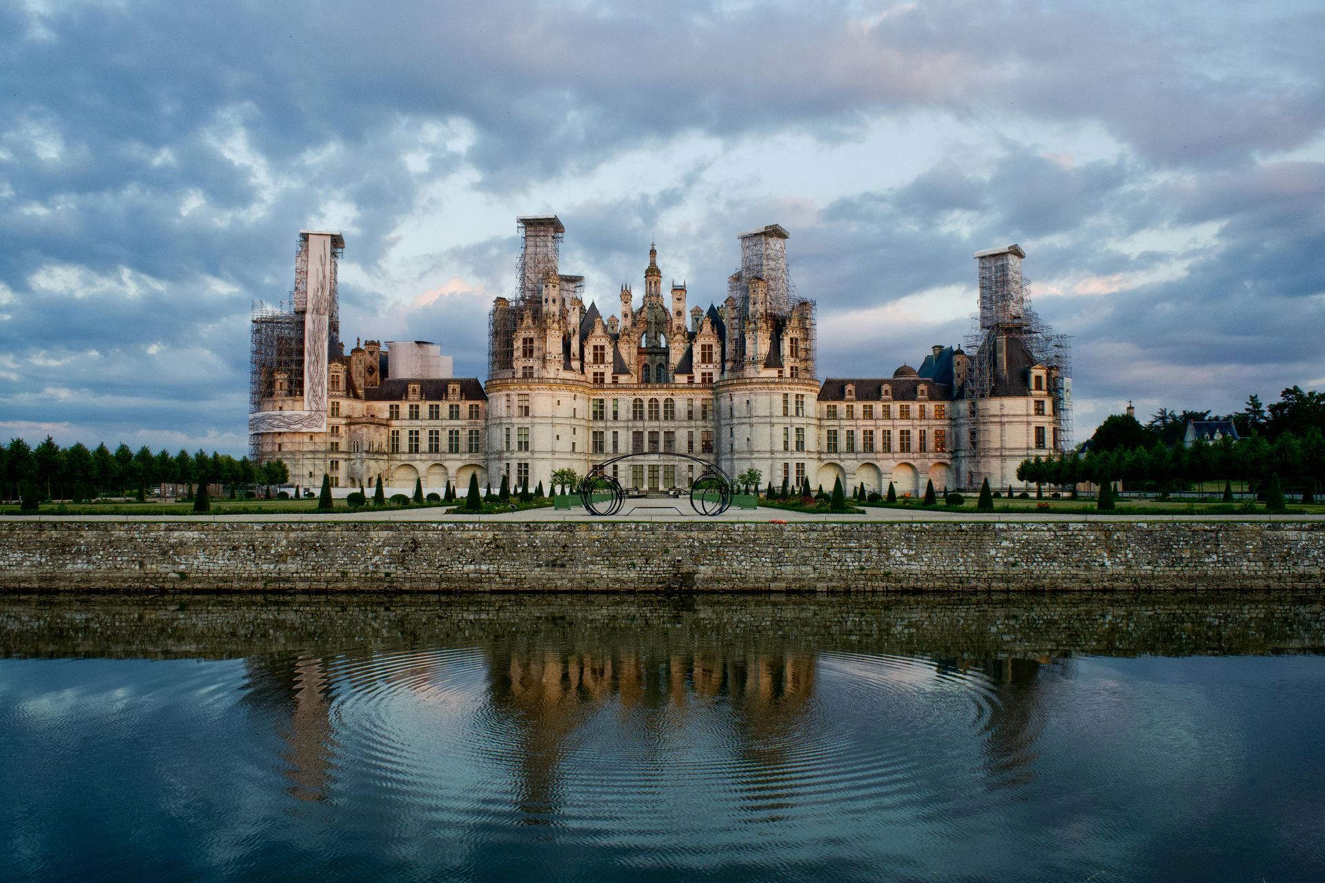 Château de Chambord reflected in water under a cloudy sky. The French Renaissance castle with scaffolding.