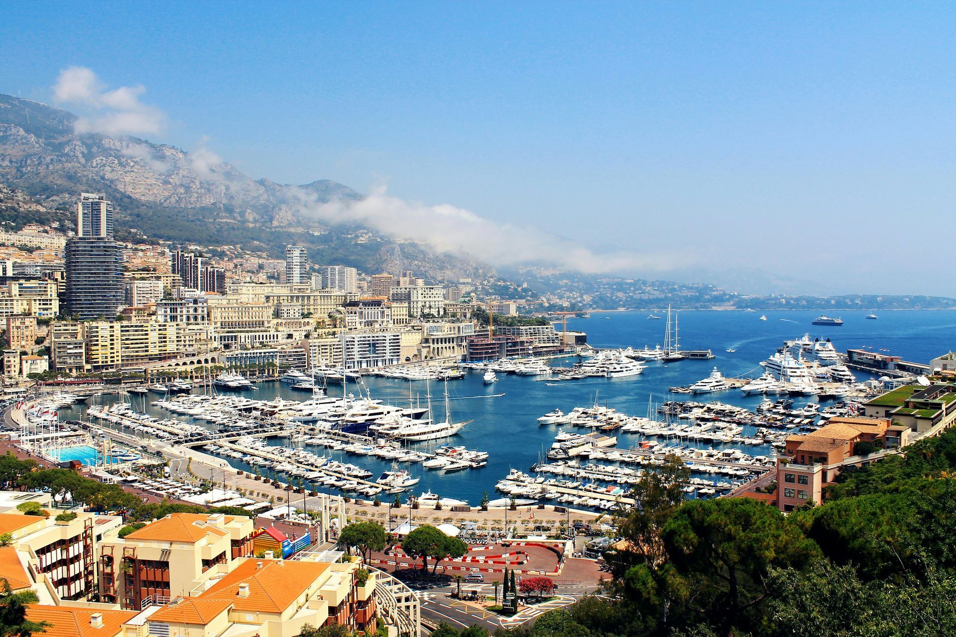 Coastal cityscape of Monaco with boats docked in harbor, buildings on hillside, and blue sky.