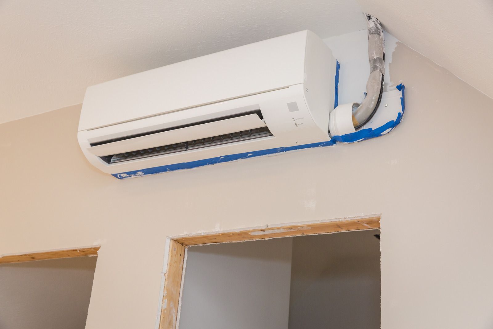 White wall-mounted air conditioner above a doorway with exposed blue wiring