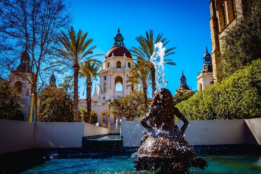 A fountain with a statue of a mermaid in front of a building and palm trees.