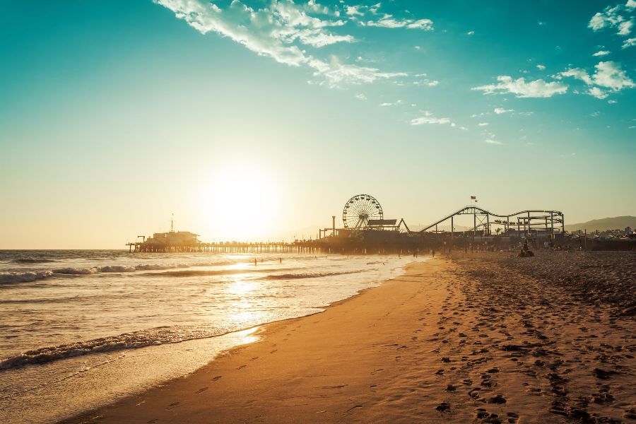 A beach with a roller coaster in the background at sunset.