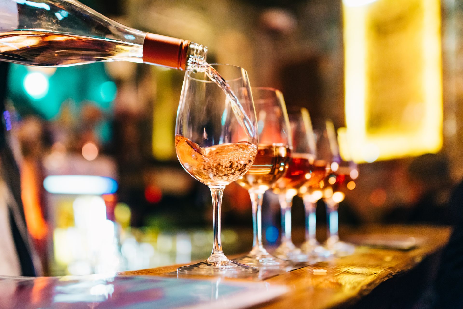 A bottle of wine is being poured into a glass on a bar.