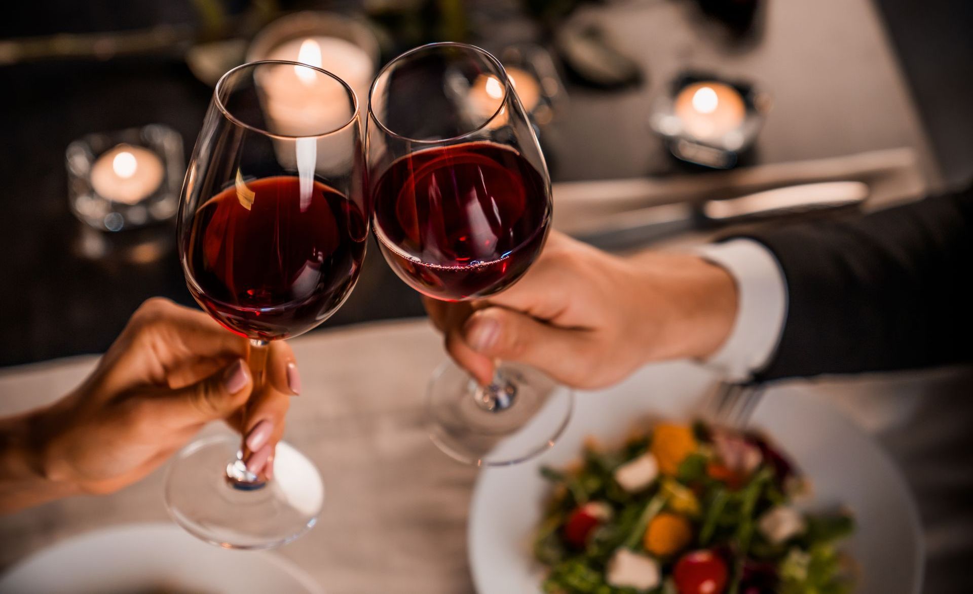 A man and a woman are toasting with wine glasses at a dinner table.