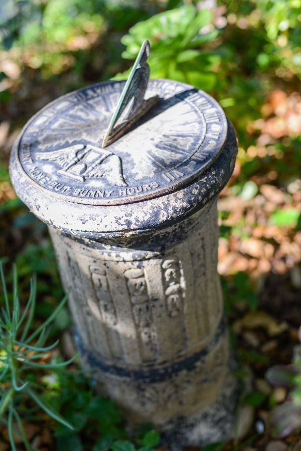 A sundial is sitting on top of a stone pillar in a garden.