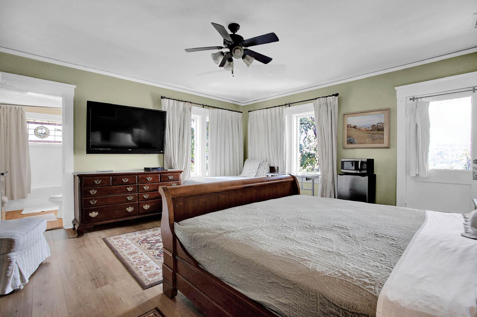 A bedroom with a king size bed , dresser , television and ceiling fan.