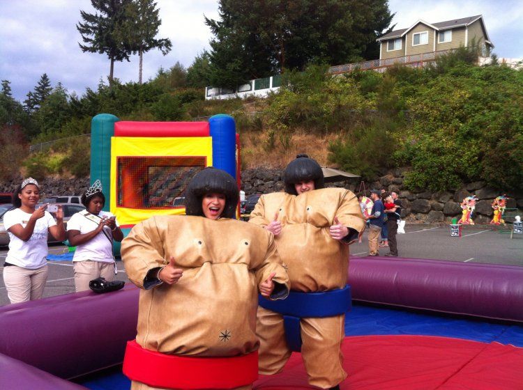 Two people in sumo suits are standing next to each other in front of a bouncy house.