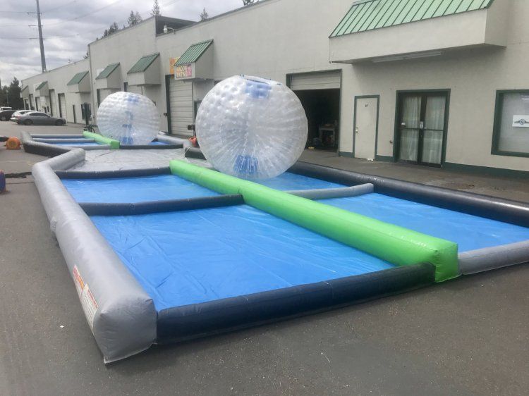 A row of inflatable water balls are sitting on top of a blue surface in front of a building.
