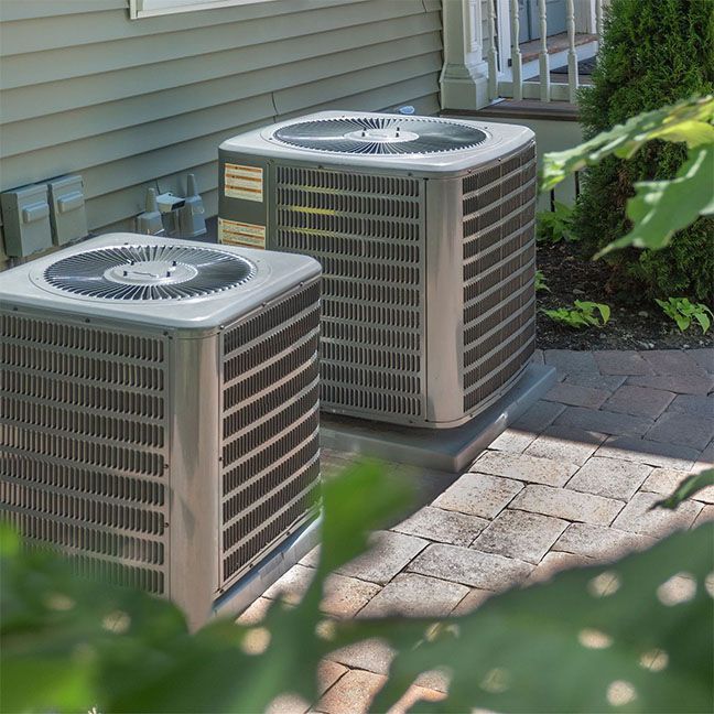 Two air conditioners are sitting on the side of a house.