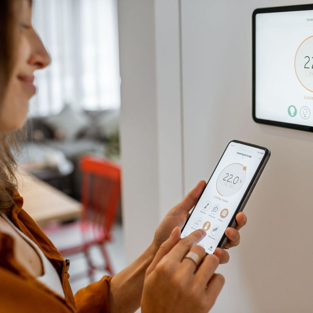 A woman is using a smart phone to control a thermostat.