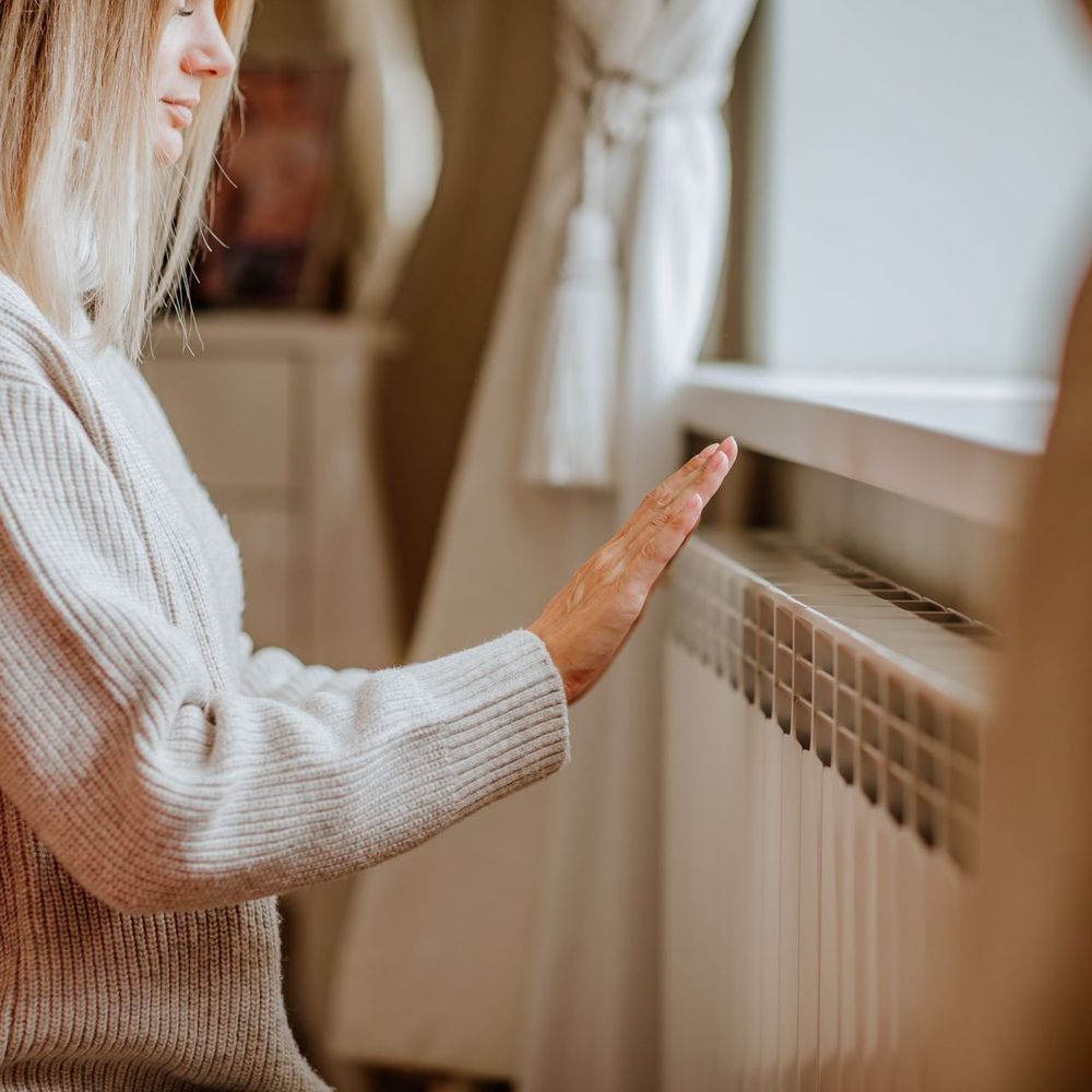 A woman in a sweater is touching a radiator with her hand.