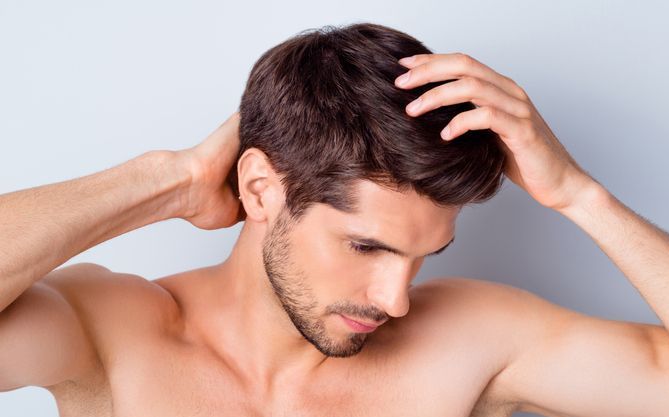 Un uomo si gratta la testa e il collo con un'espressione perplessa, sullo sfondo di un grigio chiaro.