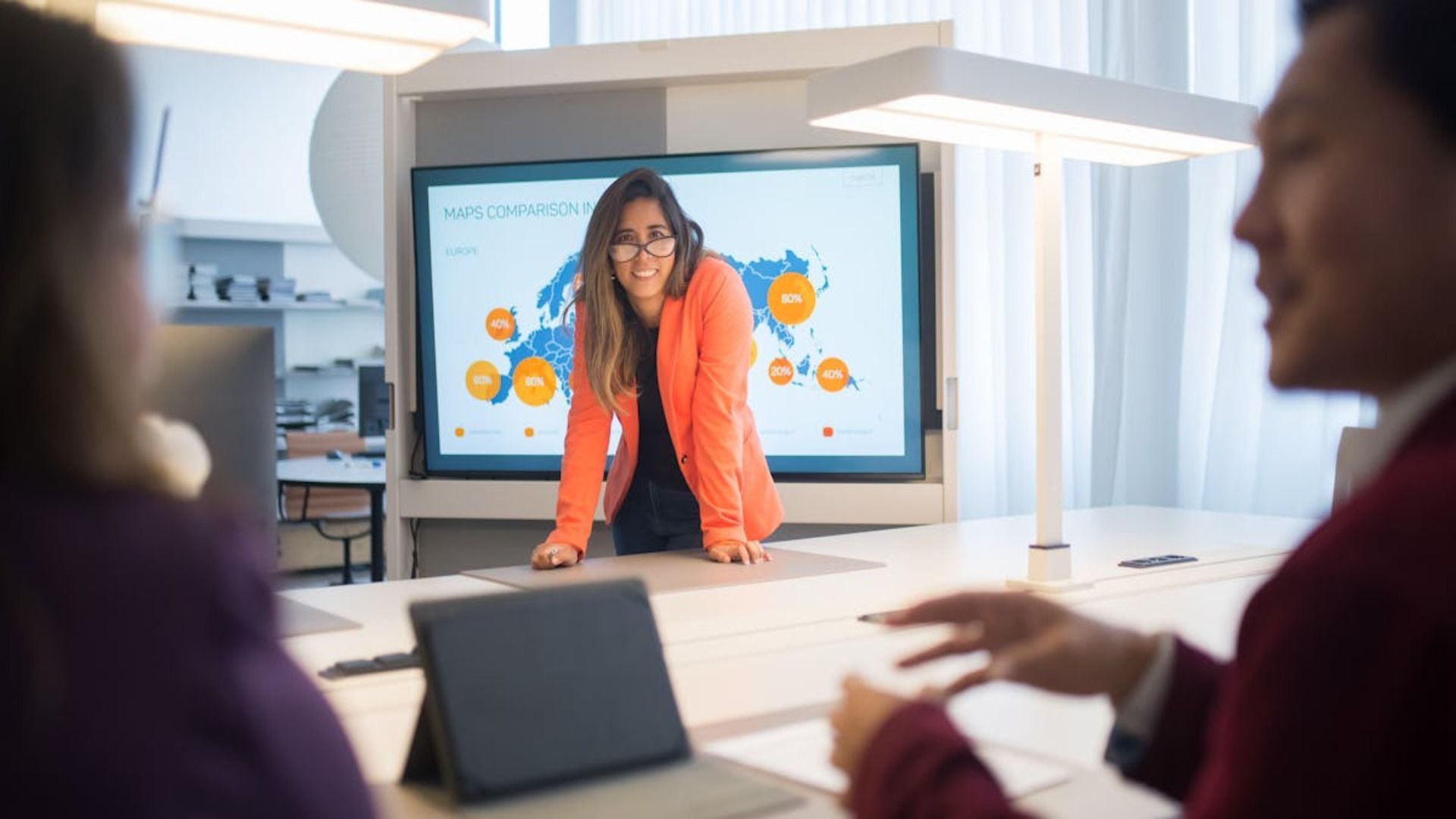 Una persona con una chaqueta naranja está de pie frente a una pantalla que muestra un mapamundi