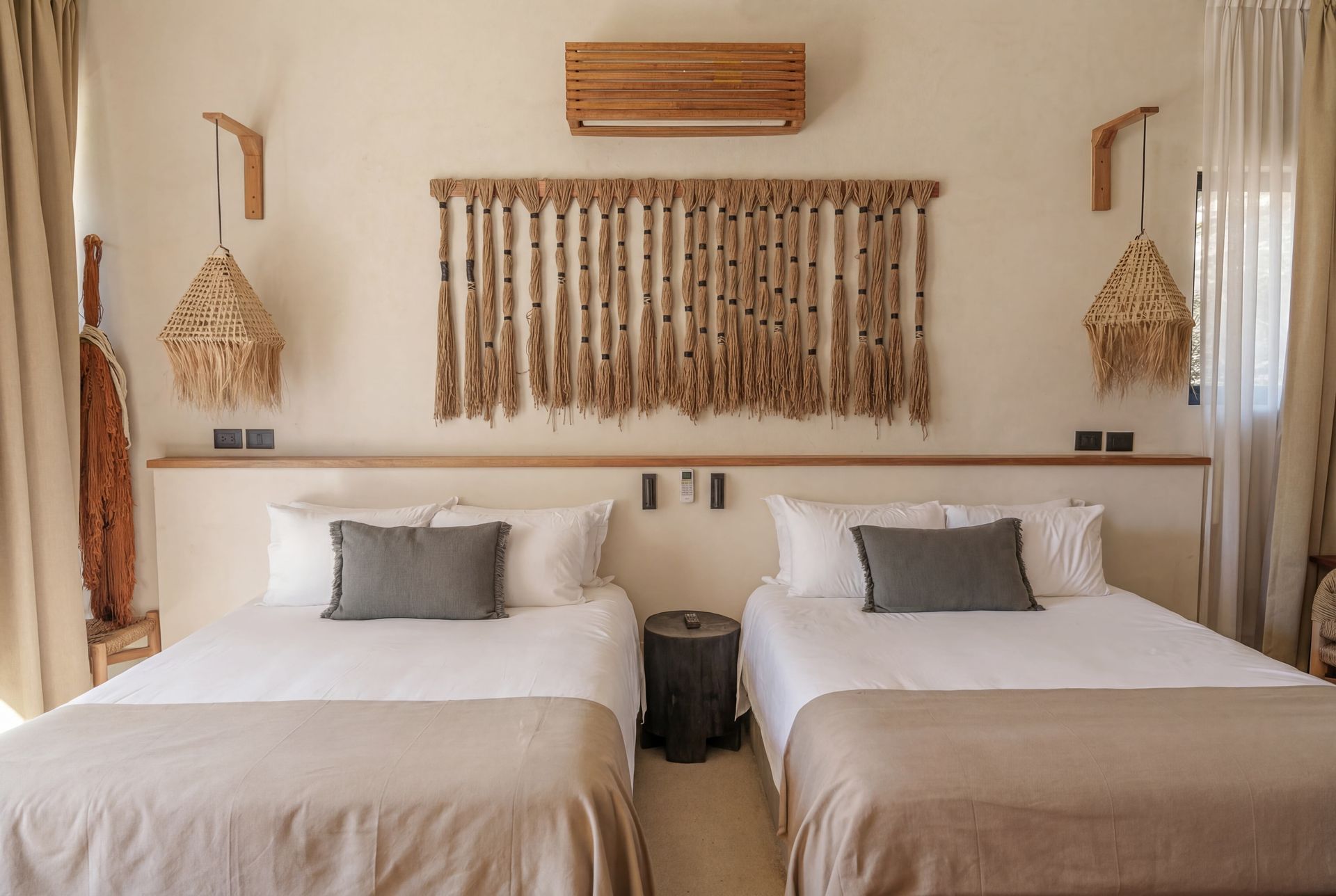 Twin beds in a beige, boho-style room with woven wall decor and a small table between them