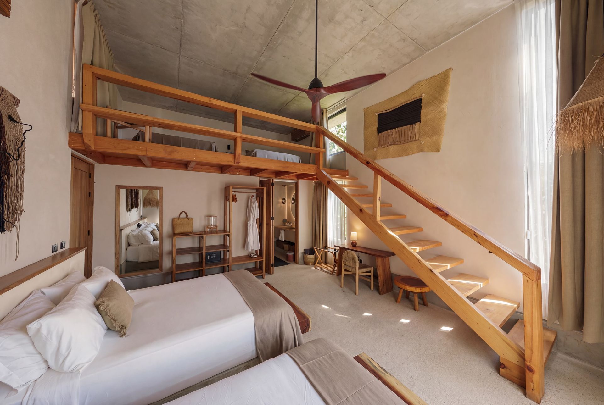 Loft bedroom with two beds, wooden staircase, and vaulted ceiling in a bright rustic room