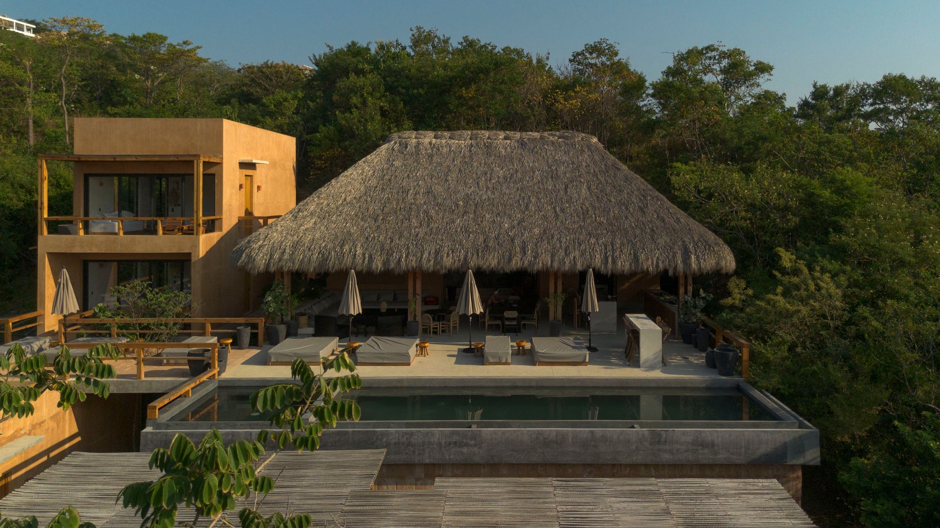 Tropical resort villa with thatched-roof pavilion, pool, and lush greenery at sunset