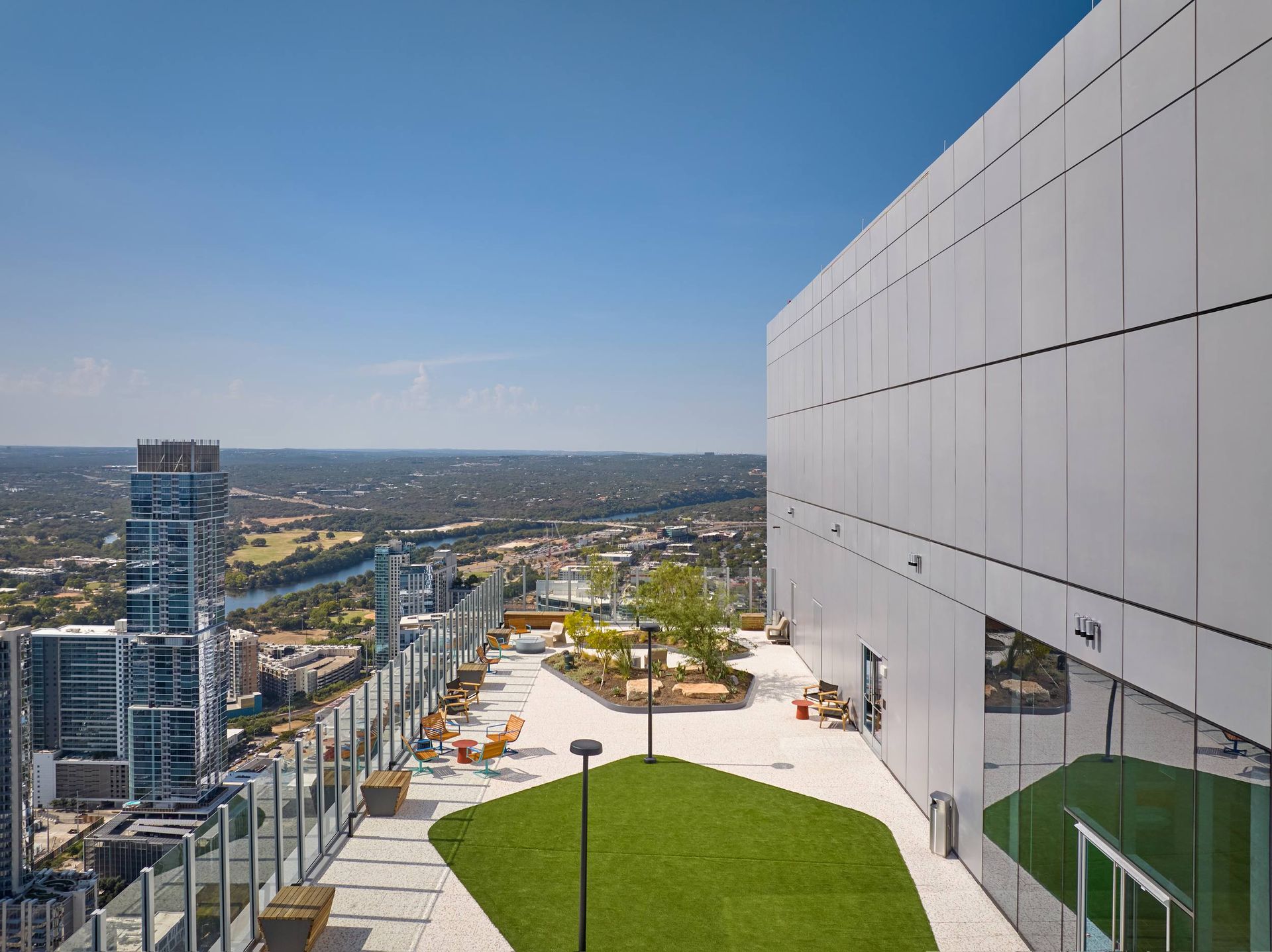 Rooftop patio with cityscape view, featuring green turf, seating, and a large white wall.