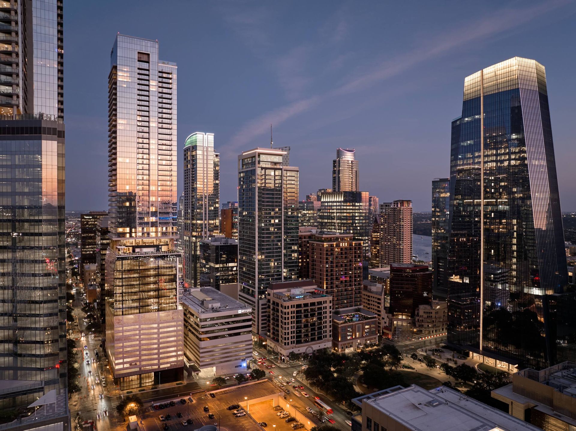 City skyline at dusk with lit skyscrapers and streetlights.