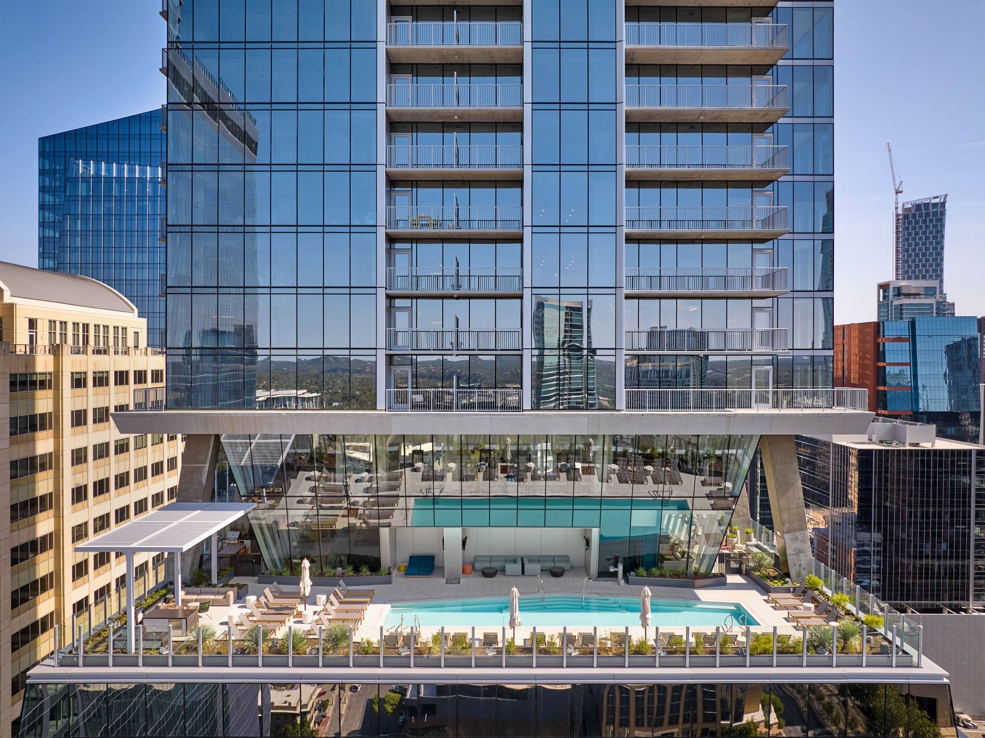 High-rise building with a rooftop pool and patio area, surrounded by city skyscrapers on a sunny day.