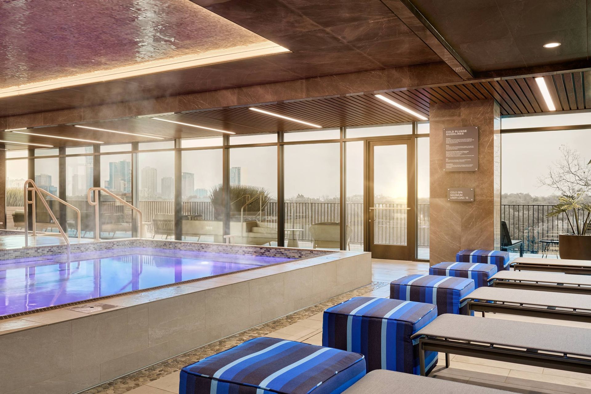 Rooftop spa with a pool, steam, lounge chairs, and city view through large windows.