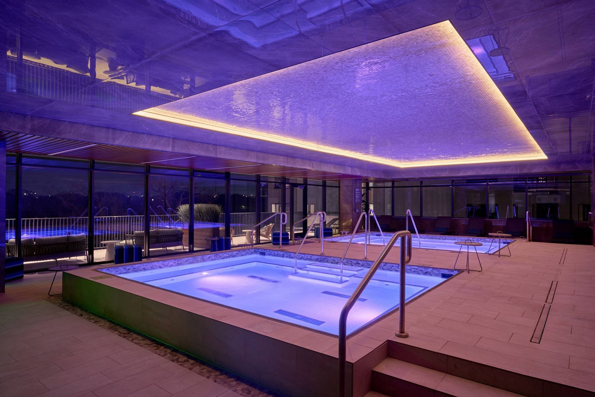 Indoor spa with rectangular pools, lit in blue. Bright, rectangular ceiling light.