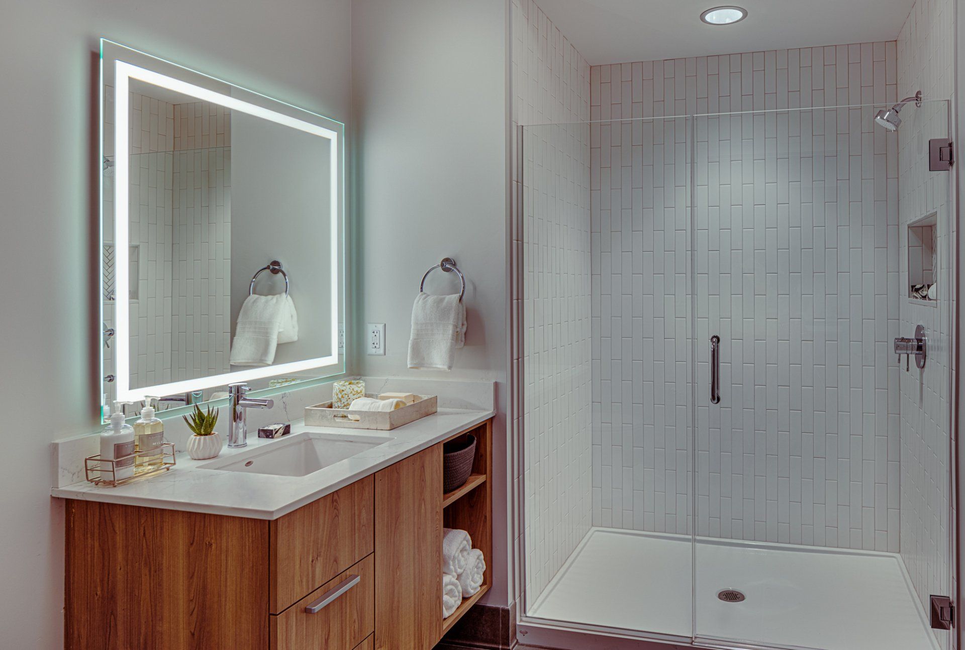 Luxury bathroom with glass shower door, mirror with light, and bathroom sink with cabinets at Gild Apartment.