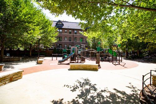 A playground in a park with a large building in the background.