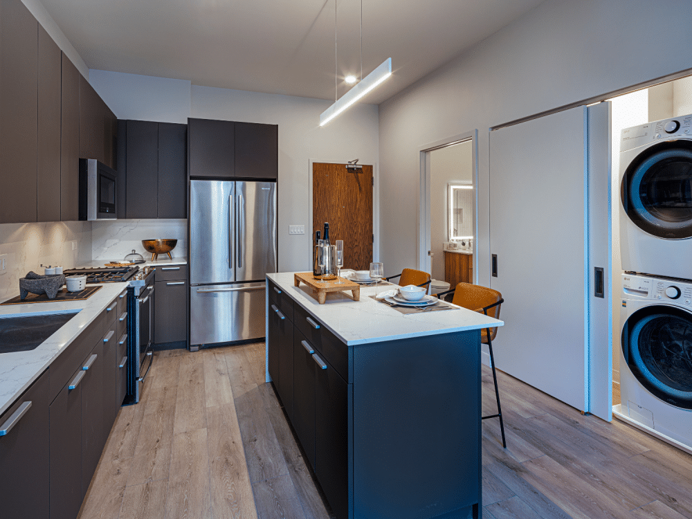 Modern kitchen with island and laundry room right next to it at Gild Apartment.