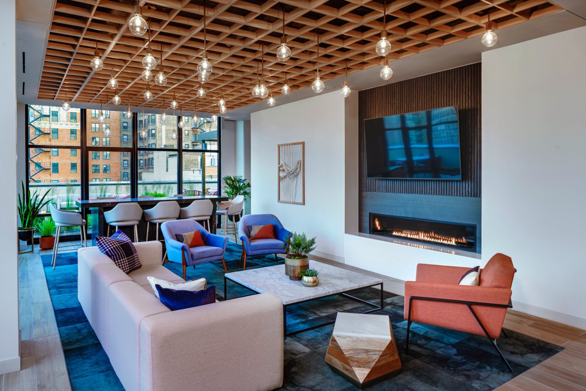 Clubhouse with wood ceiling, designer lighting, sofa, rug, and fireplace at Gild Apartment.