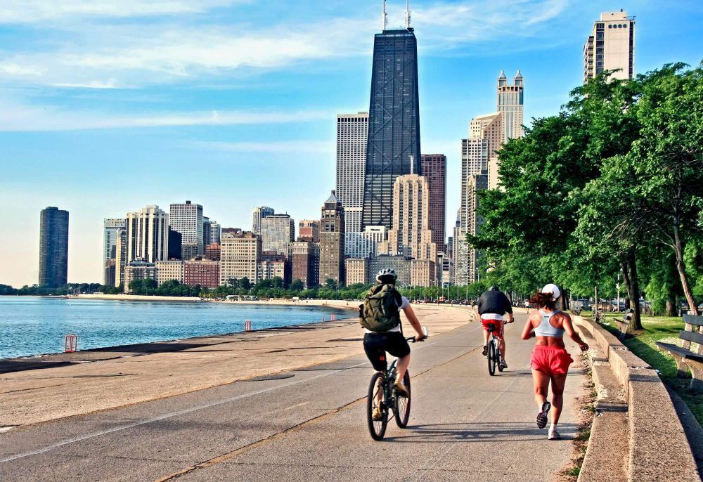 A group of people are riding bikes and running on a sidewalk in front of a city skyline.