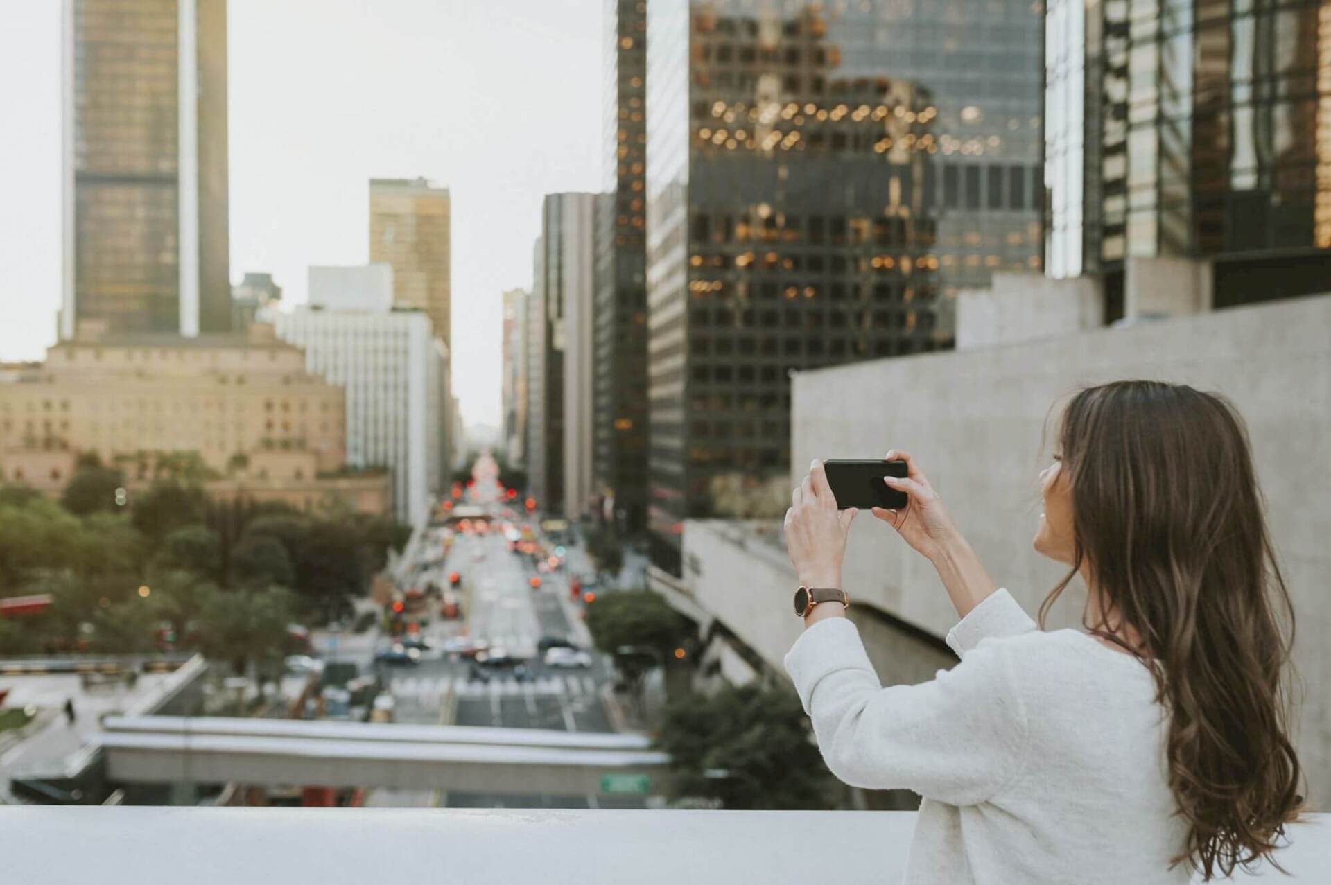 A woman is taking a picture of a city with her cell phone.