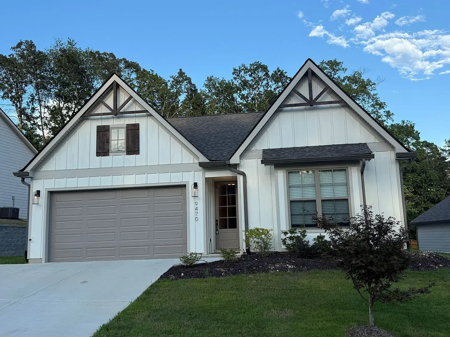 White house with gray garage door, black trim, and small front yard under blue sky.