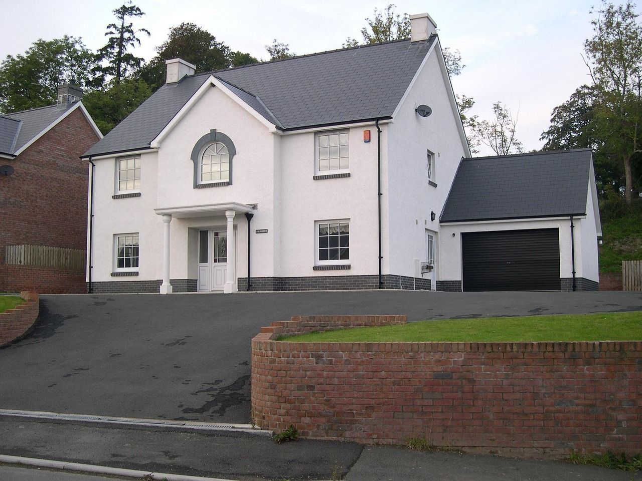 White two-story house with gray roof, attached garage, brickwork, and a paved driveway.