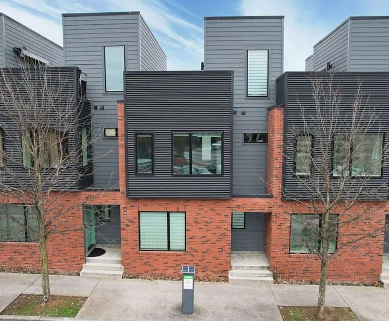 Modern townhouses with brick and gray siding, trees, and a blue sky.