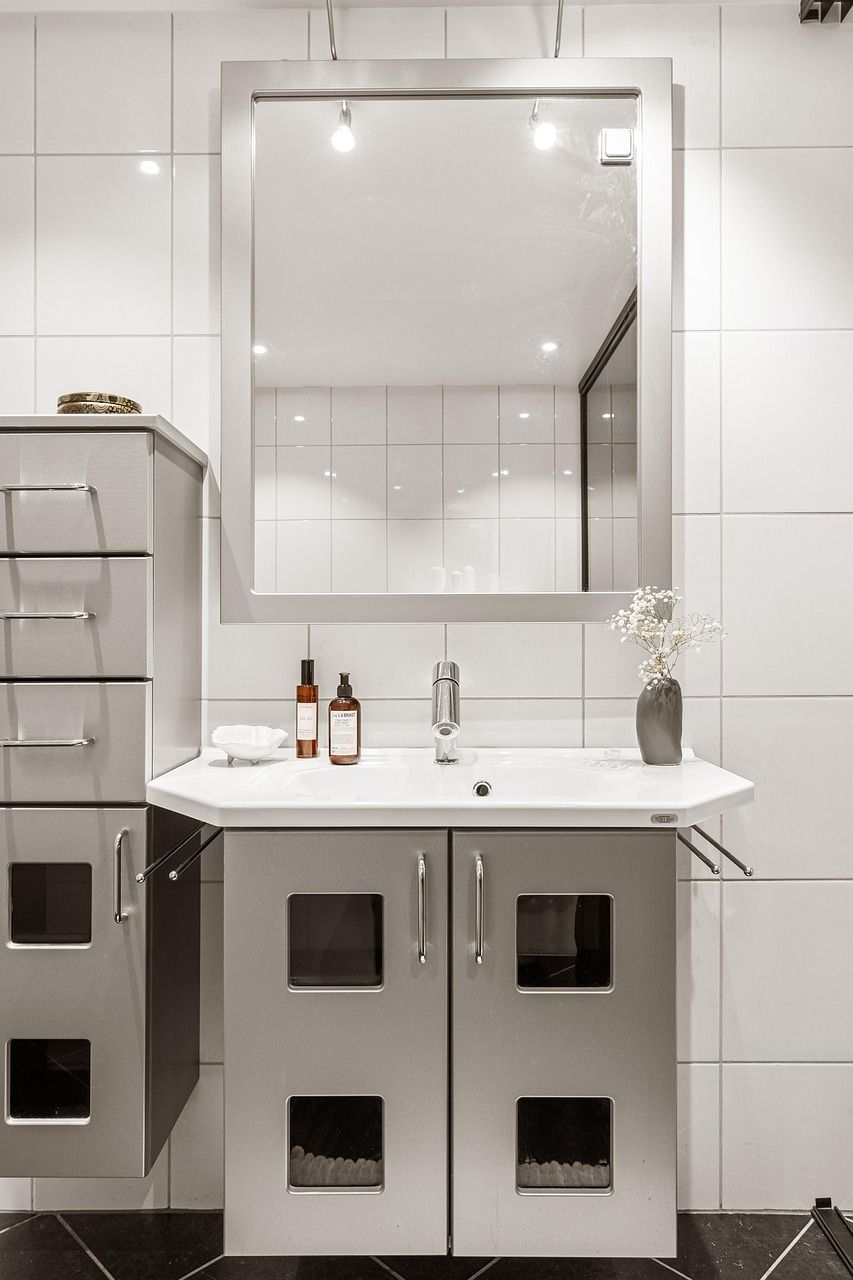 Modern bathroom with gray vanity, mirror, and white tiled walls.